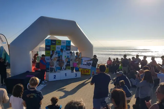 Encontro de surf do clube na praia, com participantes e público junto ao pódio.